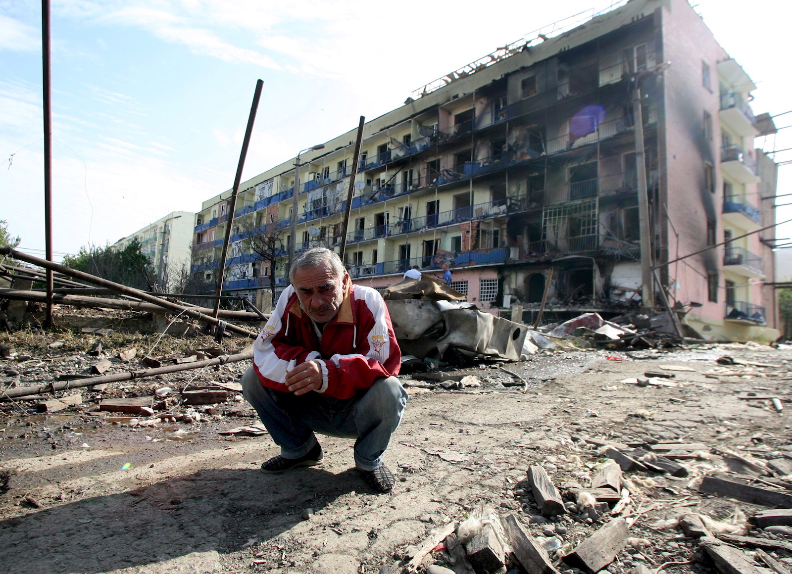 კადრში ჩანს გორელი კაცი. ფონზე დაბომბვის შედეგად დაზიანებული შენობა © EPA/ZURAB KURTSIKIDZE